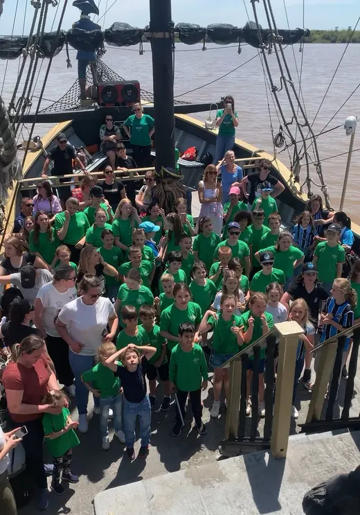Turma de alunos de camiseta verde reunida no convés do navio pirata durante o passeio pedagógico
