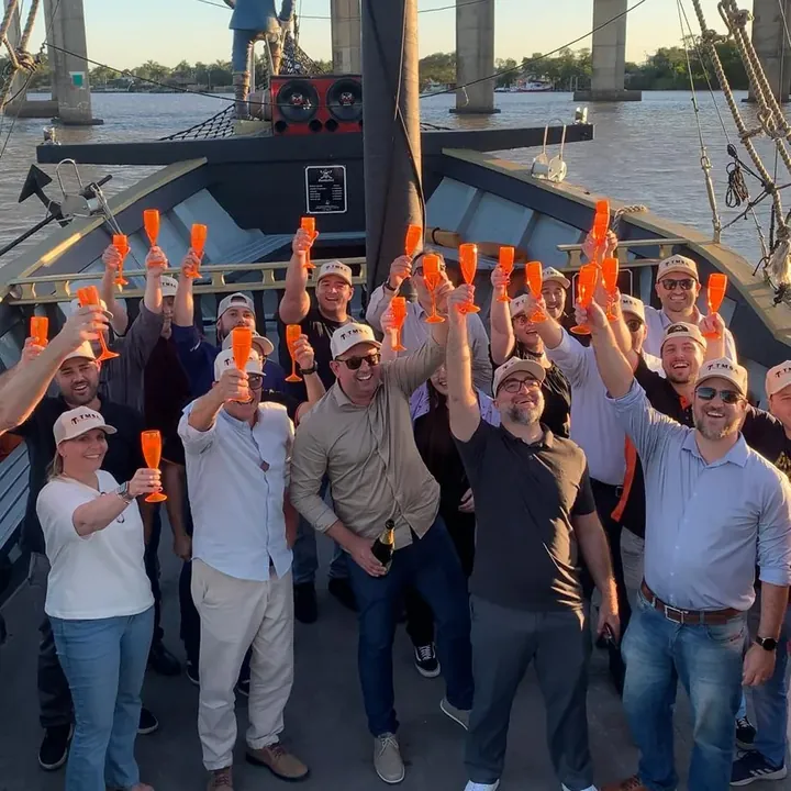 Equipe de uma empresa brindando com taças laranja no convés do navio pirata